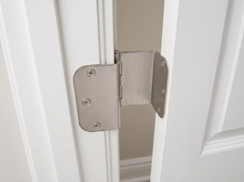Close-up of a brushed metal offset door hinge installed on a white wooden door, showing the wide swing clearance.
