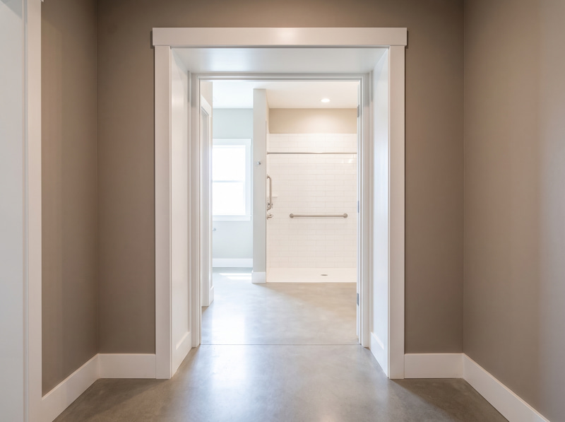 View from a clean hallway through a newly widened doorway into an accessible bathroom with a step-free shower and grab bar.